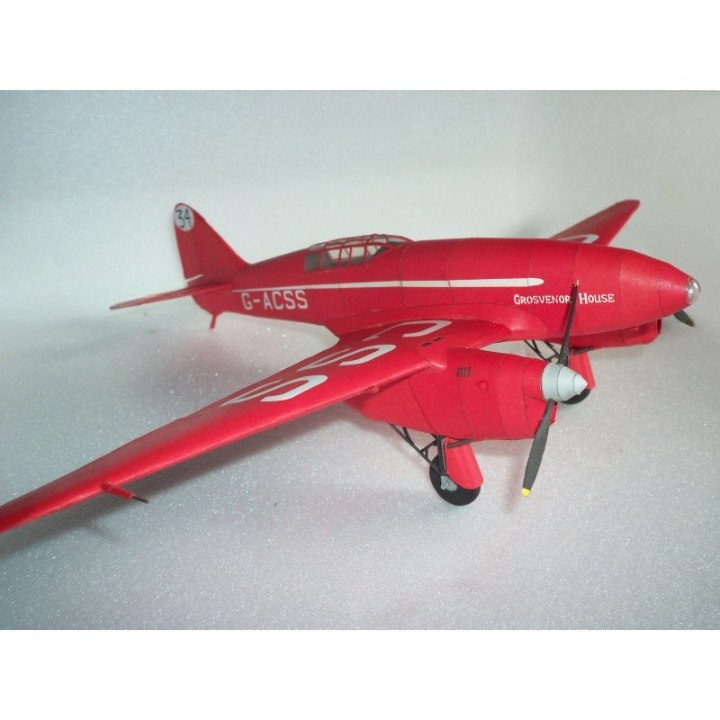 A red model airplane with white markings and a silver propeller, photographed on a light gray textured surface.