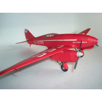 A red model airplane with white markings and a silver propeller, photographed on a light gray textured surface.