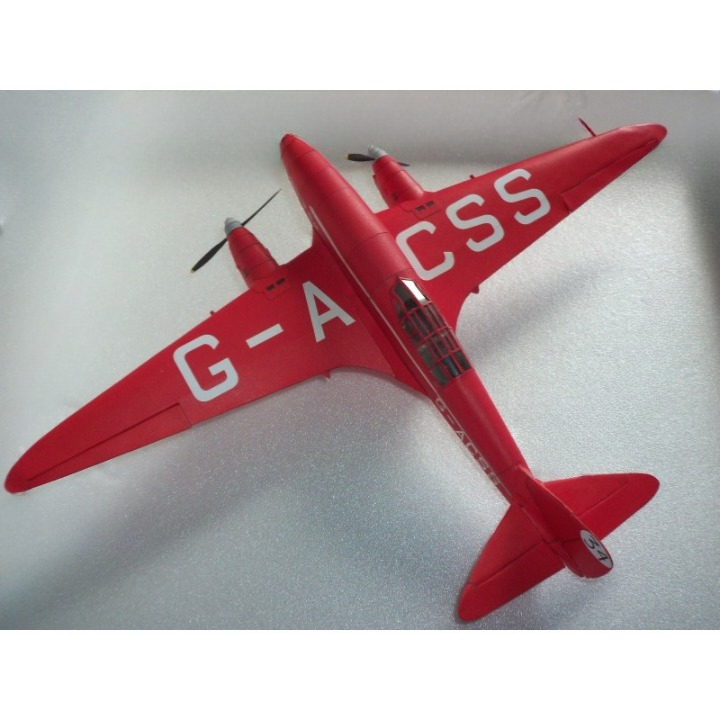 A red model airplane with white lettering reading G-A CSS on the wings and fuselage, photographed on a light gray textured background.