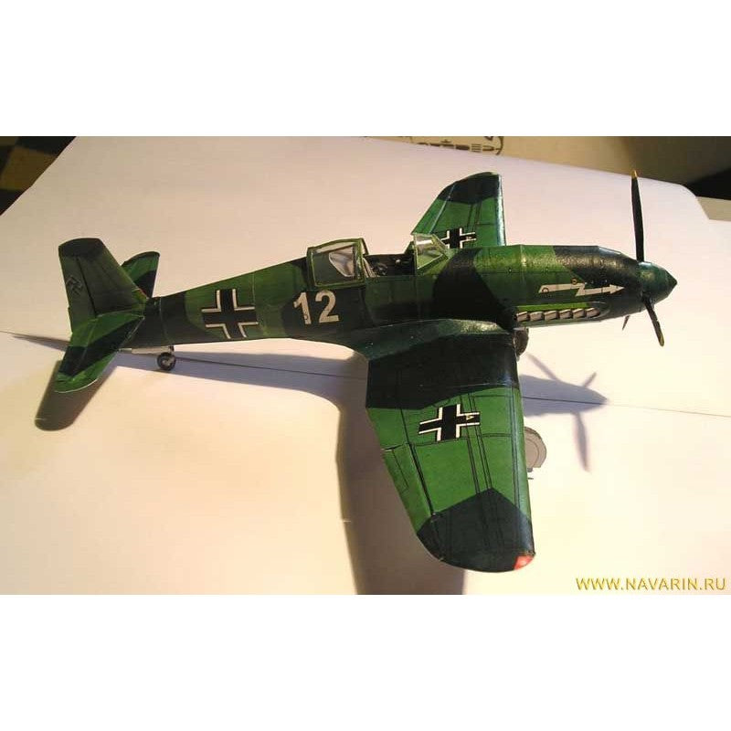 A model of a German WWII fighter plane, likely a Junkers Ju 87 Stuka, painted in a green and black camouflage scheme with white German Iron Cross markings and the number 12. The model is photographed on a white surface with a visible shadow.