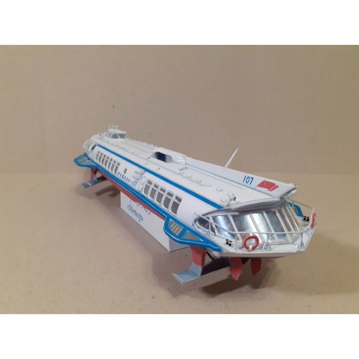 A vintage toy model of a passenger liner, resembling the RMS Titanic, displayed on a beige background. The model is primarily white with blue and red stripes, detailed windows, and a silver metallic bridge.