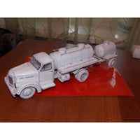 An unpainted white miniature model of a tanker truck, displayed on a red sheet of paper over a wooden table.