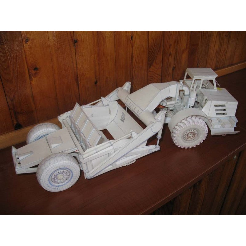 A white assembled wooden building block model of a front-end loader truck with a dump bed, displayed on a wooden shelf against a wooden wall.