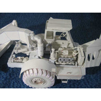 An unpainted white plastic model of a heavy-duty truck or loader, shown from a three-quarters angle on a textured blue background.
