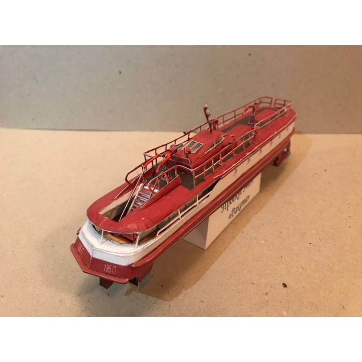 A red and white model ferry or passenger boat displayed on a small support stand against a plain beige background.