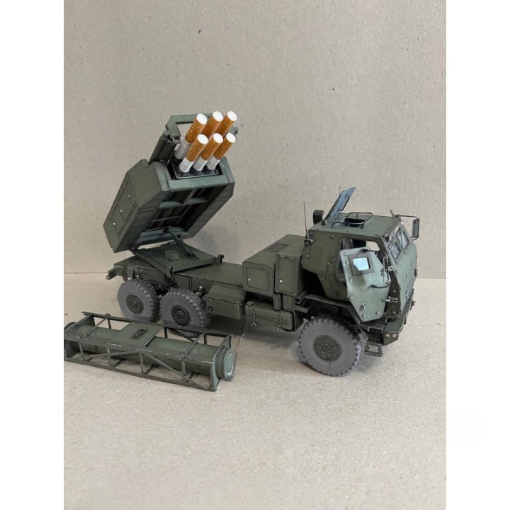 A scale model of an olive green military missile launcher truck with its launcher raised, shown on a neutral beige background.