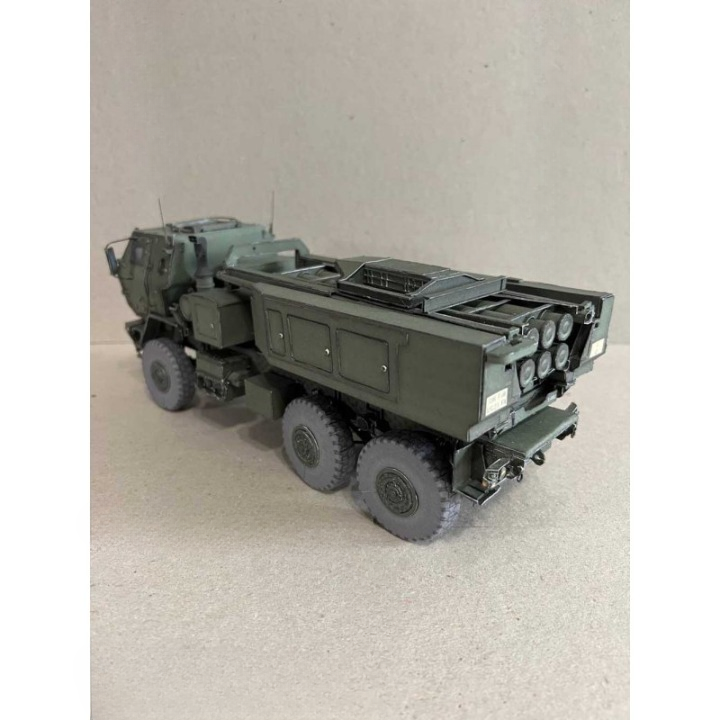A detailed model of an olive green military truck with a missile launcher on a light beige textured surface.