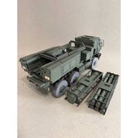 A detailed military model truck with a cargo bed carrying multiple cylindrical missiles, shown alongside separate missile launcher components on a plain beige background.