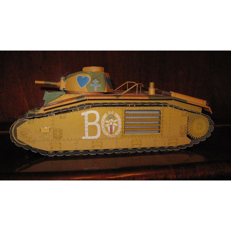 A vintage toy or model tank in a desert tan color, decorated with a blue heart, white letter 'B', and a crest on the side, displayed against a dark wooden background.