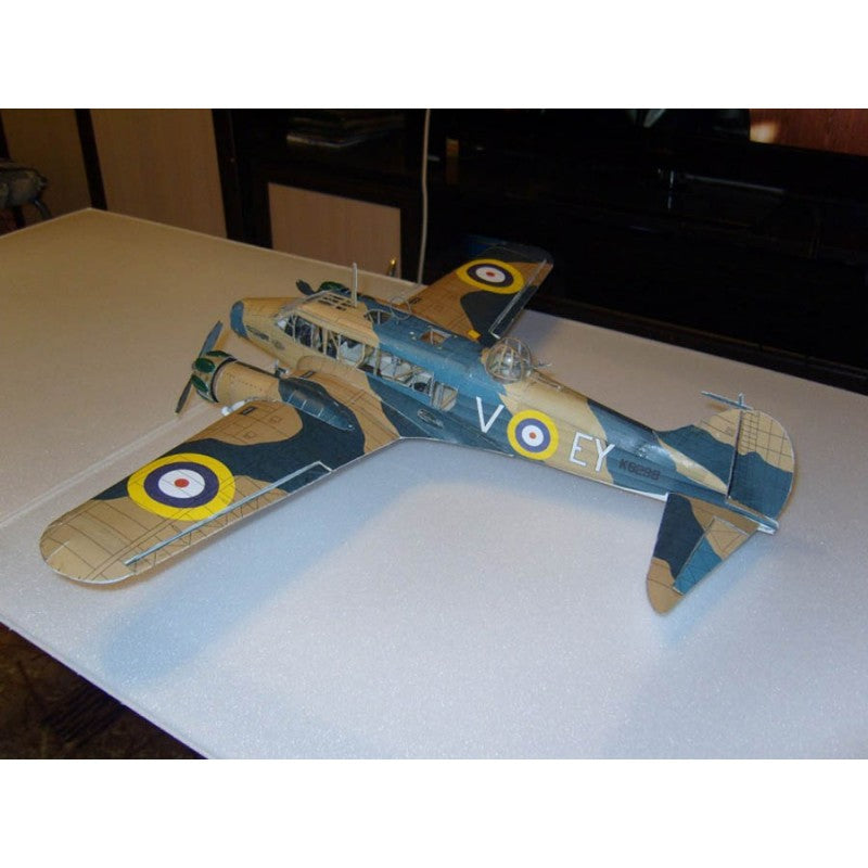 A vintage-style model airplane with a camouflage pattern in tan, green, and dark gray, featuring roundel markings and white lettering on the fuselage, displayed on a light-colored tabletop.