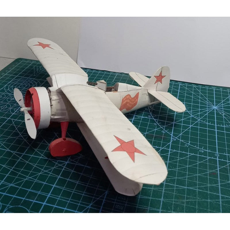 A small white and red model airplane with star decals, placed on a green cutting mat.
