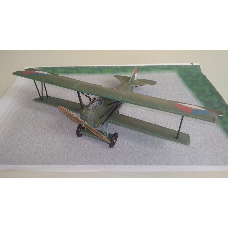 A scale model of a vintage military biplane in olive green with red, white, and blue roundel insignias on the wings, displayed on a textured gray surface with a green printed backdrop.