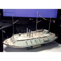 A detailed model of a military ship displayed on a desk in front of a computer monitor and keyboard.