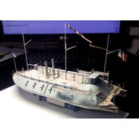 A detailed model of a historic steamship, likely a US Navy vessel, displayed on a white surface against a dark background with a computer monitor visible in the distance.