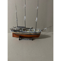 A detailed model of the historic sailing ship Barataria, built with a brown wooden hull, dark gray upper deck, and multiple black masts, displayed on a black stand with a label.