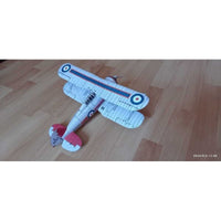 A small model biplane toy with a white body, blue and red striping, and roundel markings, placed on a light wood floor.