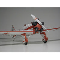 A scale model of a vintage red and white airplane with a white propeller, photographed on a neutral gray studio background.