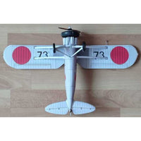 A small model or toy biplane viewed from above on a light wood surface. The plane is mostly white with two large red circular markings on the wings and black printed numbers '73' on each wing.