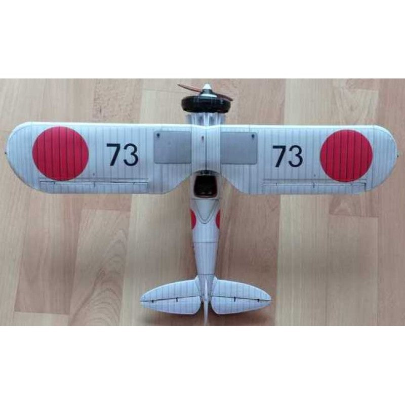 A small model airplane photographed from above on a light wood floor. The plane is white with two large red circular markings and the number 73 printed in black on each wing.