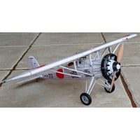 A silver and white Japanese military-style model airplane with a wooden propeller, black wheels, and red and black markings, photographed on a concrete surface.