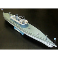 A detailed model of a vintage ocean liner or cargo ship, shown at an angle on a dark background. The model features a light gray hull and deck, a blue-gray superstructure, silver smokestacks, and black railings.