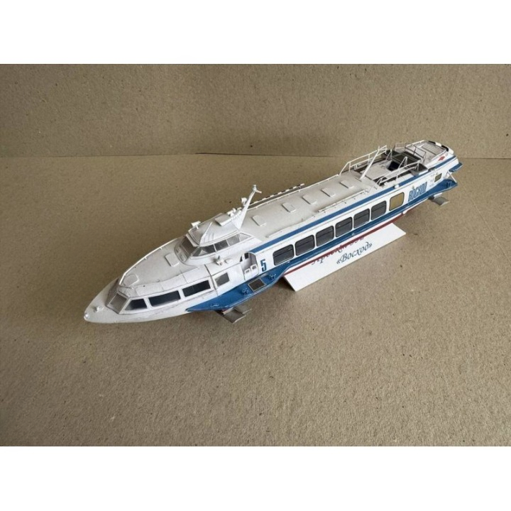A white and blue model ferry or passenger ship displayed on a small stand against a plain beige background.