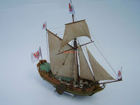 A detailed model of a historical three-masted sailing ship with beige sails, a brown wooden hull, and white flags featuring red and blue heraldic designs, set against a plain light gray background.