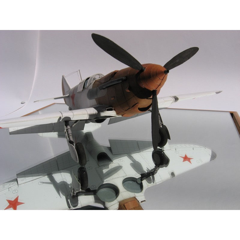 A detailed model of a vintage military fighter plane with a brown and gray fuselage, black propeller blades, and red star insignias on a light gray background.