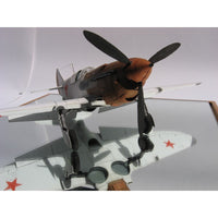 A detailed model of a vintage military fighter plane with a brown and gray fuselage, black propeller blades, and red star insignias on a light gray background.