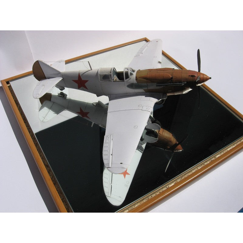 A vintage-style model airplane displayed on a mirrored surface inside a wooden frame. The aircraft is primarily white with brown sections on the nose and propeller, and red star insignias on the wings and fuselage.