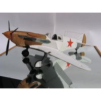 A scale model of a vintage military fighter airplane with a brown and white camouflage fuselage, red star insignia on the side, and a black propeller, displayed on a stand against a light gray background.