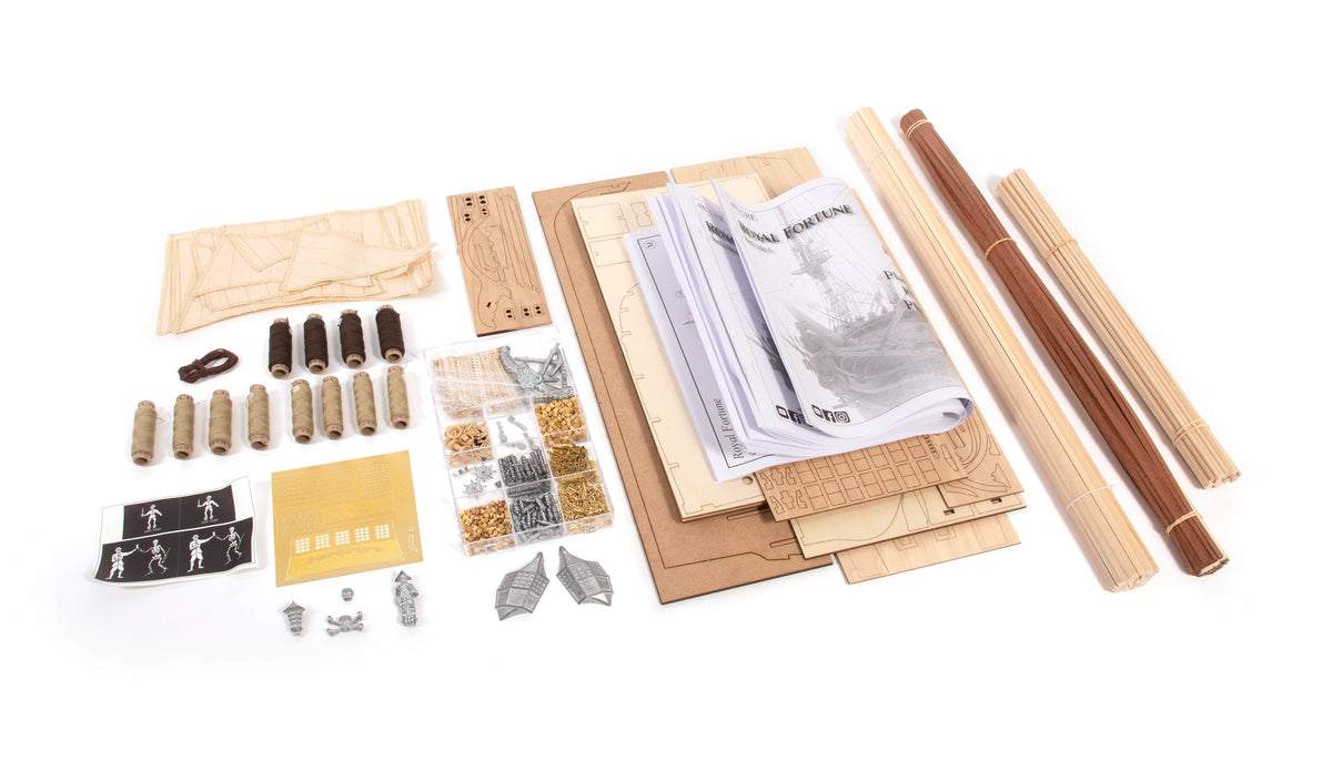 A flat-lay view of a miniature model kit components and accessories on a white background, including wooden rolling mats, small metal hardware, miniature figures, and a printed instruction booklet.