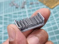 Small plastic model with miniature components held between fingers on a grid background