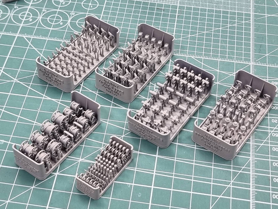Set of small model figures in gray color on a green cutting mat with grid lines.