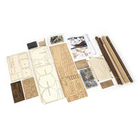 A flat-lay view of a wooden model kit or furniture assembly set, showing various pre-cut wooden panels, dowels, hardware, and instruction sheets on a plain white background.
