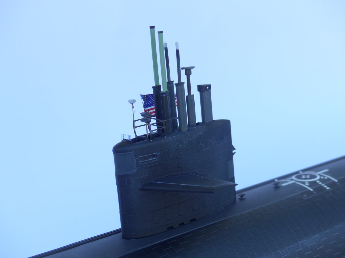 Model of a submarine with antennas and an American flag against a clear blue sky