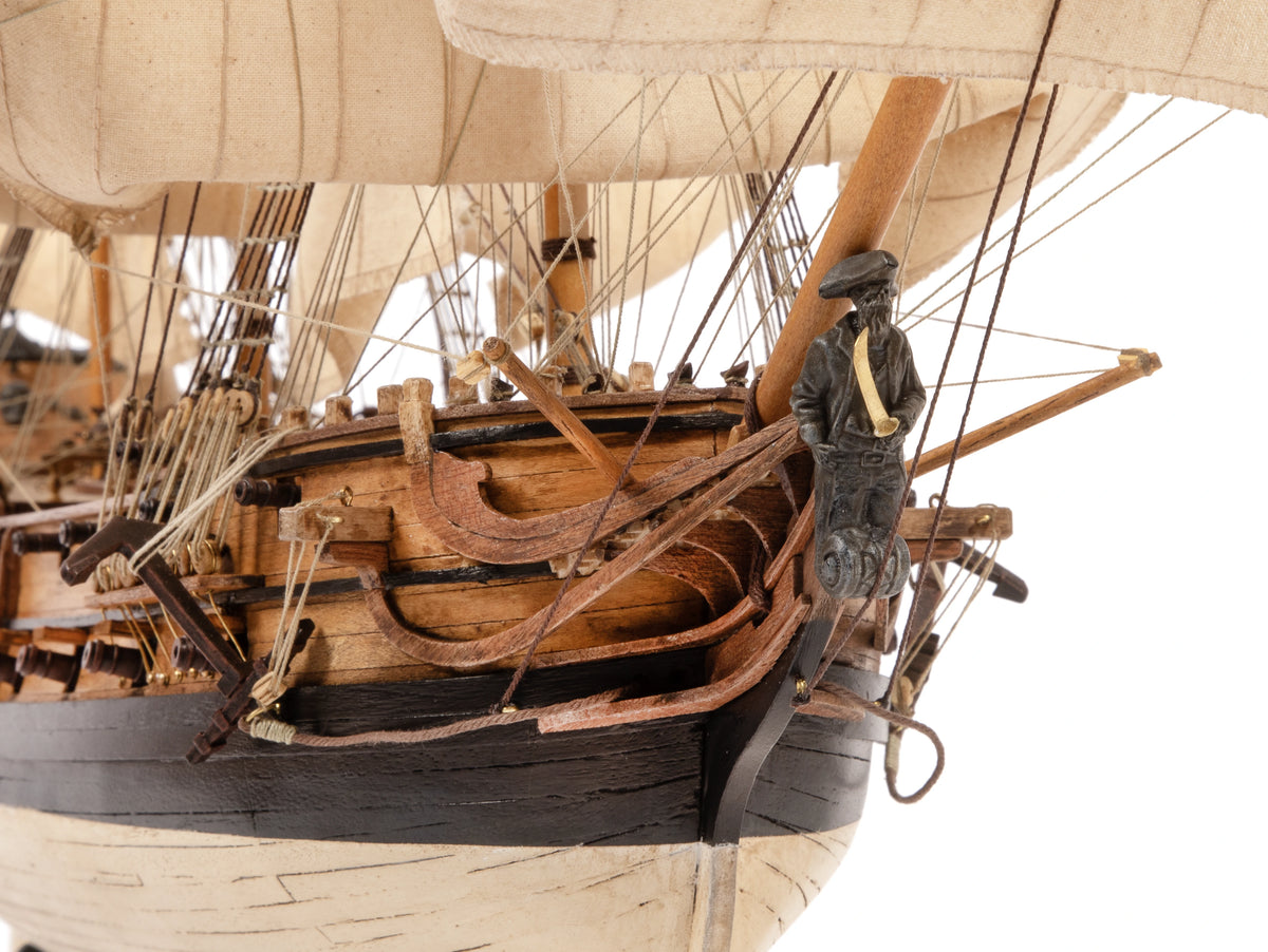Close-up of a wooden model ship with detailed rigging and a figure on a white background