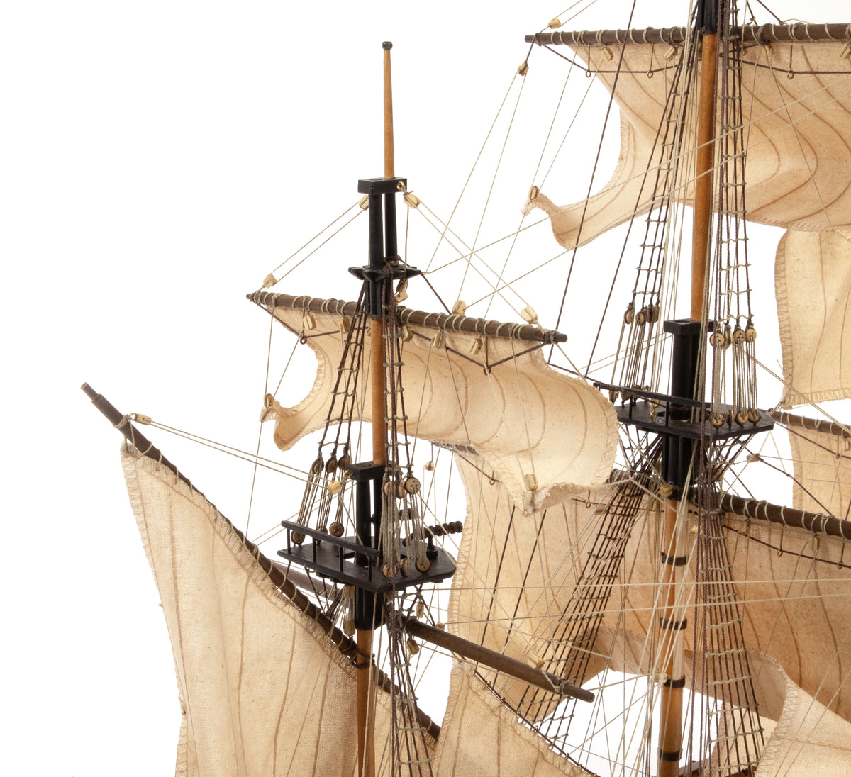 Close-up of a detailed model or replica of a historical three-masted sailing ship with beige canvas sails, wooden masts, and rigging against a plain white background.