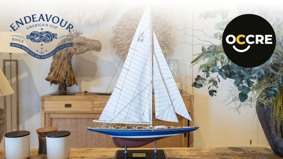 Photo of the OcCre Endeavour America's Cup yacht model kit in 1:75 scale, showing detailed wooden hull, rigging, and classic sail design.