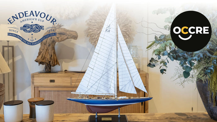 Photo of the OcCre Endeavour America's Cup yacht model kit in 1:75 scale, showing detailed wooden hull, rigging, and classic sail design.
