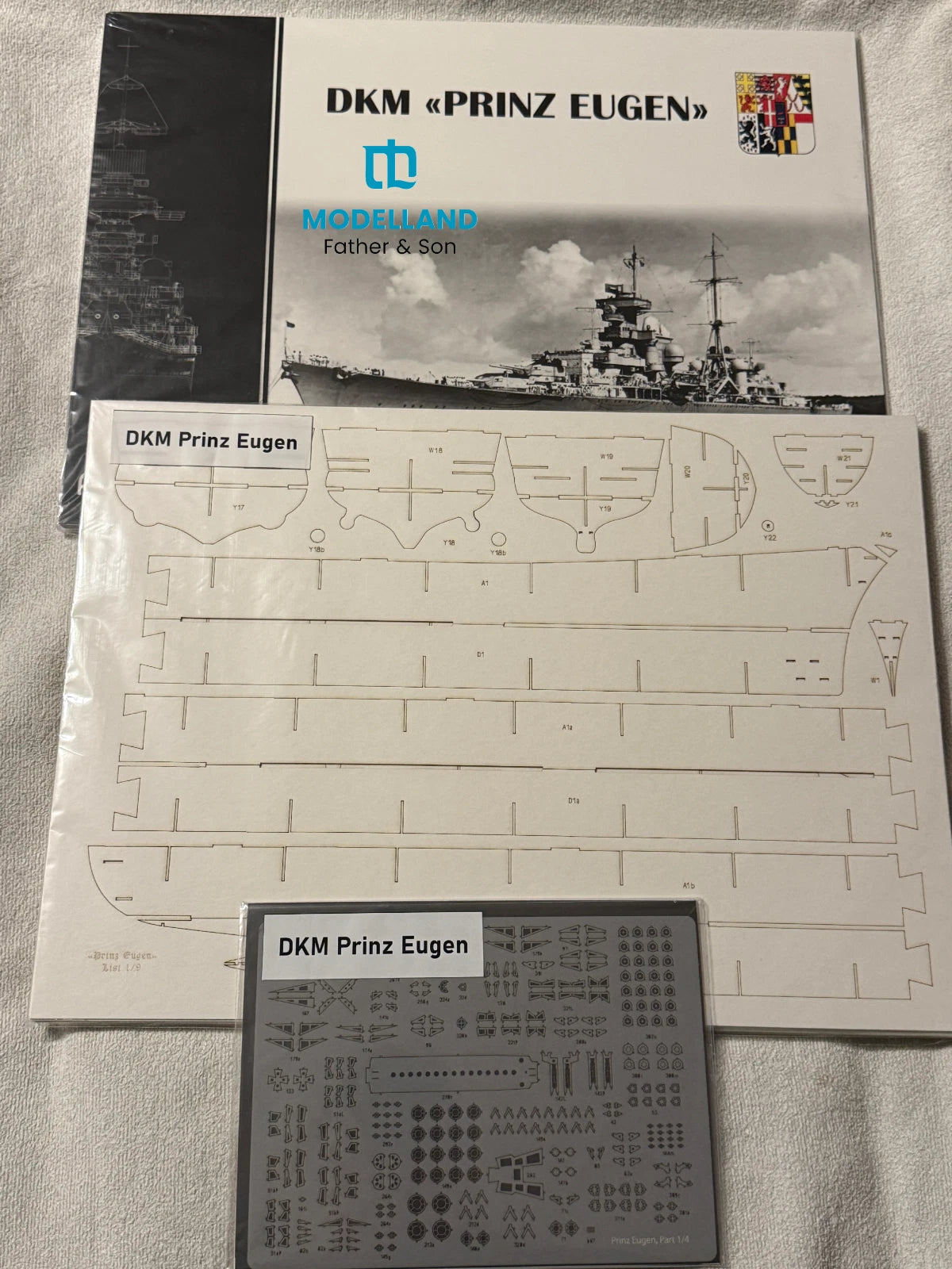 Model kit parts kit for the German battleship DKM Prinz Eugen, including the main instruction booklet, a sheet of cut-out templates, and a sheet of small metal decals, all branded with the 'Moreland' logo.