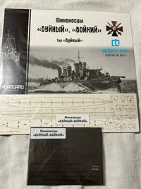 Model kit packaging and accessories laid out on a light fabric surface, including a box cover with a ship photo and Russian text, a sheet of decals, and a dark instruction sheet. Visible branding includes ModelLand and Avancard.