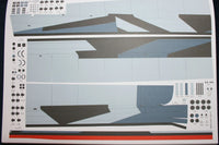 A sheet of model kit decals or transfer stickers featuring a gray and blue aircraft fuselage design with various printed markings, logos, and symbols on a white backing sheet.