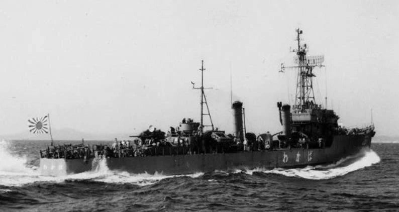 Black and white historical photograph of a Japanese military ship at sea, with a large crowd of people visible on the deck and a Japanese sun flag flying at the stern.