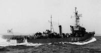 Black and white historical photograph of a Japanese military ship at sea, with a large crowd of people visible on the deck and a Japanese sun flag flying at the stern.