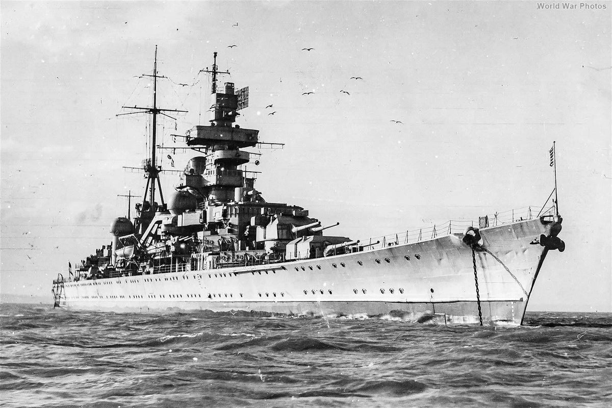 Black and white historical photograph of a large naval battleship at sea, with birds in the sky and a faint 'World War Photos' mark in the upper right corner.