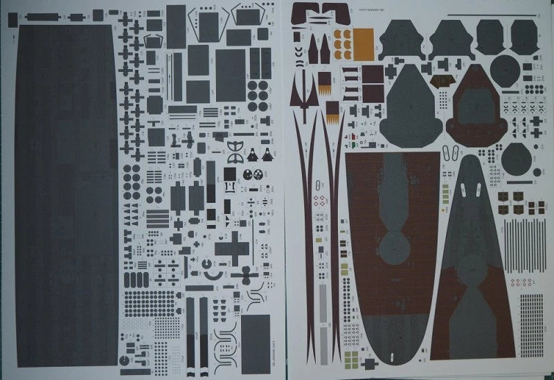 A sheet of model kit decals or transfer stickers laid flat on a white background, featuring various shapes, logos, and graphic elements in dark gray, black, brown, and small orange accents.