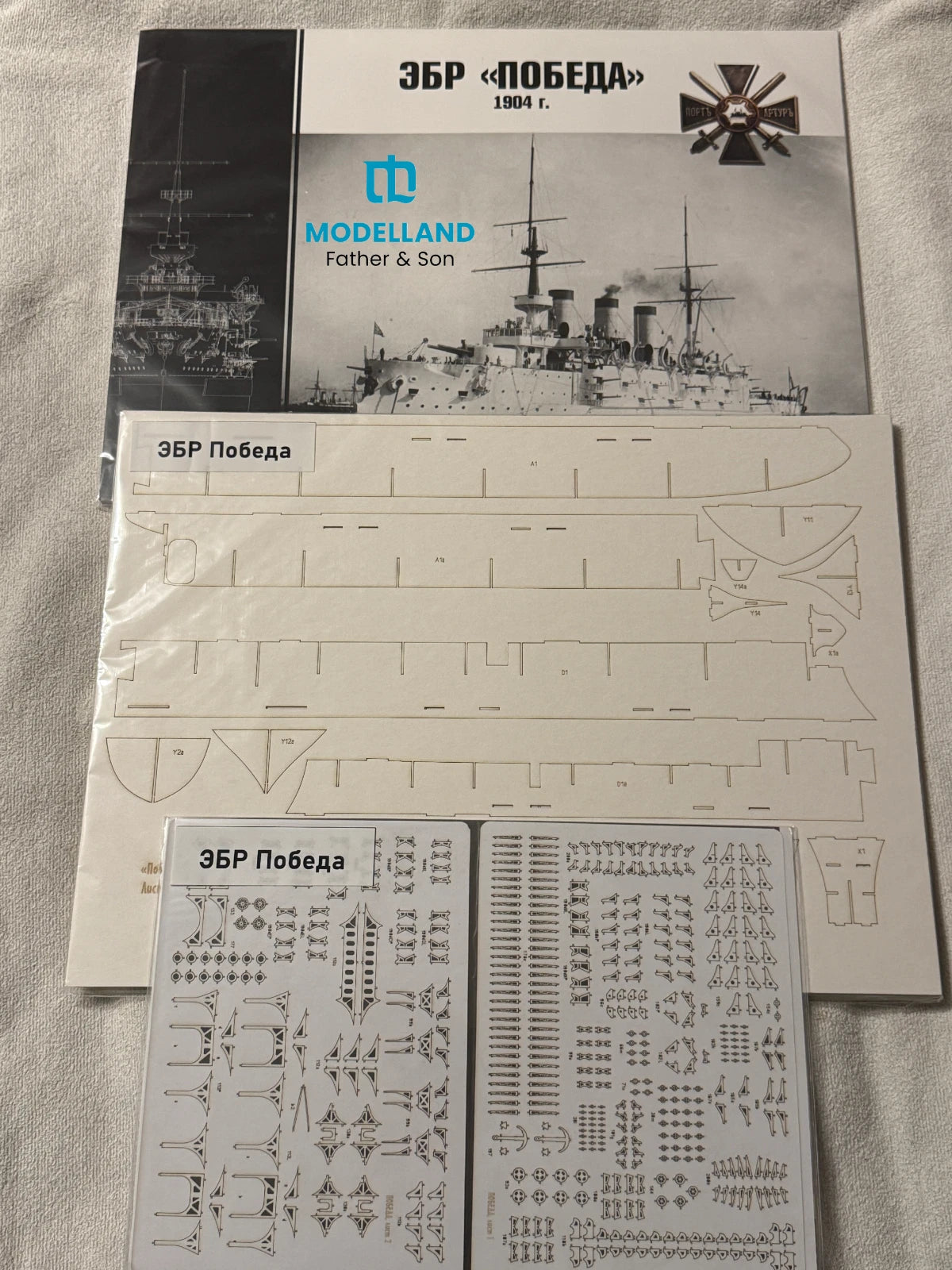 Model kit parts sheet and decal sheet for a historical Russian battleship, displayed on a light fabric background with the instruction booklet visible behind it.