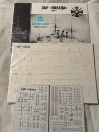 Model kit parts sheet and decal sheet for a historical Russian battleship, displayed on a light fabric background with the instruction booklet visible behind it.
