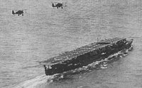 Black and white historical photograph showing an aircraft carrier at sea with two biplanes flying overhead.